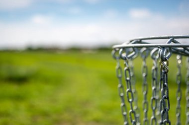 Disk golfü gol zincirleri rüzgarda yavaşça sallanıyor ve arka planda yeşil bir saha var.