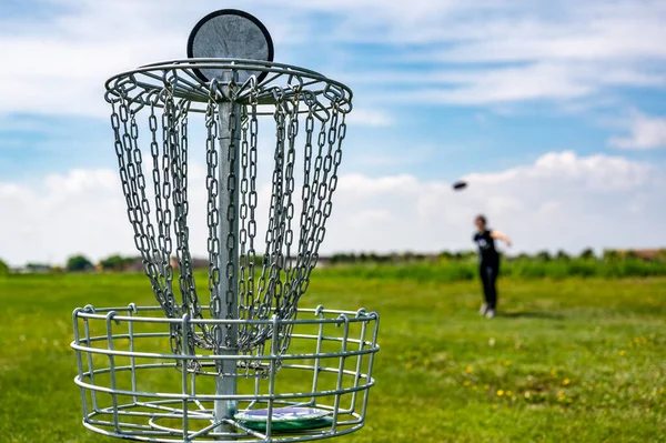 Soustřeďte se na golfovou jamku, zatímco disk je ve vzduchu poté, co byl hozen rozostřeným hráčem — Stock fotografie