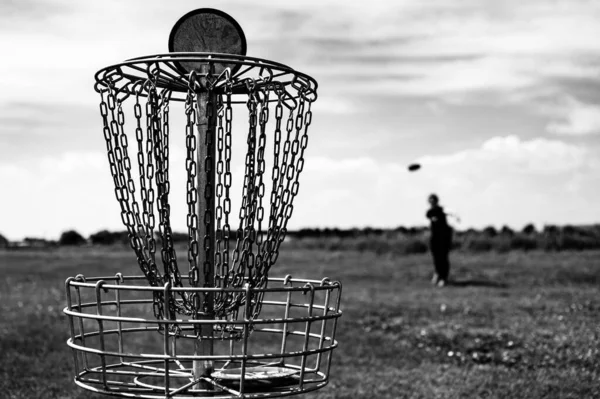 Concentre-se em um buraco de golfe enquanto o disco está no ar depois de ser jogado por um jogador desfocado — Fotografia de Stock