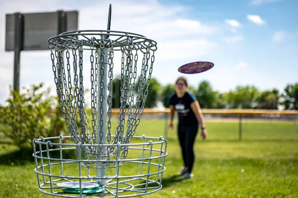 Concentre-se em um buraco de golfe enquanto o disco está no ar depois de ser jogado por um jogador desfocado — Fotografia de Stock