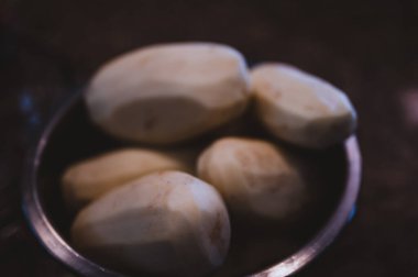 Dilimlenmeye ve pişirilmeye hazır metal bir kasede soyulmuş patateslere odaklan.