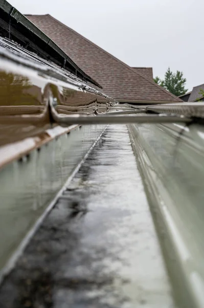 Selectieve focus op een deel van residentiële dakgoot met hanger die water transporteert tijdens een storm. Regenspetters en -druppels zichtbaar. — Stockfoto