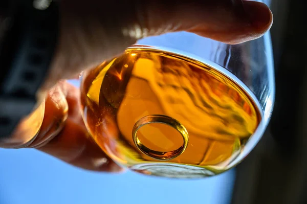 Kaukasische Hand hält ein Glas bernsteinfarbene Flüssigkeit mit einem Ehering am Boden — Stockfoto