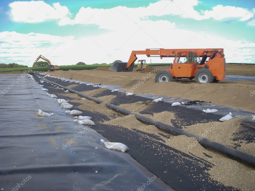 Installation of a leachate collection system under a new landfill with a liner and perforated rock.