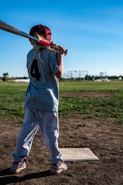 Young girl with ponytail practicing swinging a baseball bat.