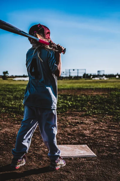 Young girl with ponytail practicing swinging a baseball bat.