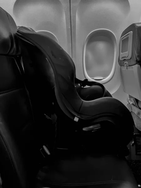 Assento de carro infantil colocado ao lado de uma janela em um avião — Fotografia de Stock