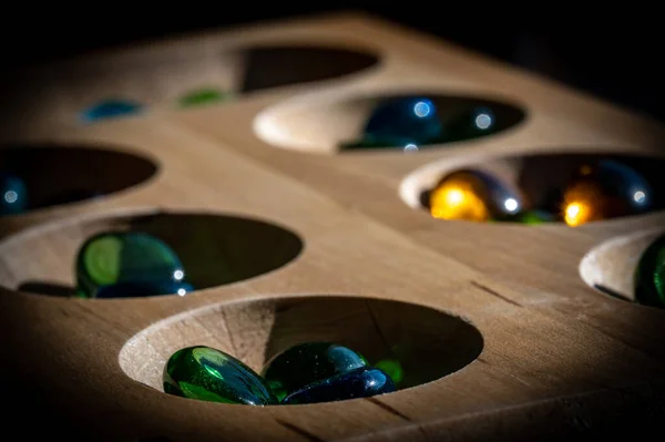 Foco seletivo em contas de vidro em uma placa de mancala de madeira — Fotografia de Stock