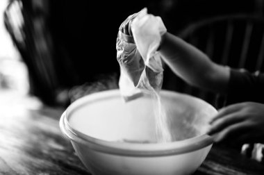 Küçük çocuk malzemeleri bir kaseye boşaltıyor ve havaya toz salıyor..