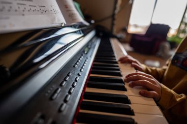 Küçük çocuk piyano çalma alıştırması yapıyor, elleri tuşların üzerinde dinleniyor.