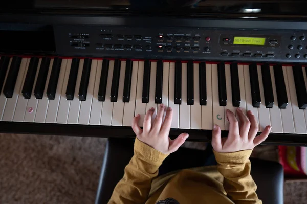 Niño pequeño que practica tocar un piano con las manos apoyadas en las teclas — Foto de Stock