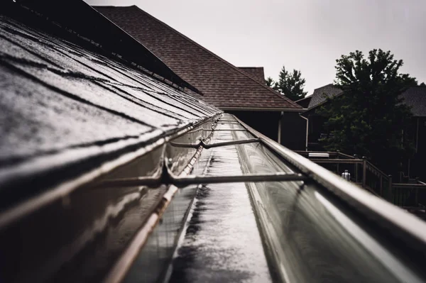 Selectieve focus op een deel van residentiële dakgoot met hanger die water transporteert tijdens een storm. Regenspetters en -druppels zichtbaar. — Stockfoto