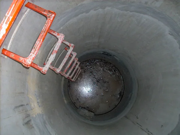Patrząc w otwarty betonowy właz ze szczeblami prowadzącymi w dół stagnacji wody — Zdjęcie stockowe