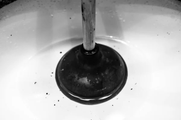 Utilisation d'un piston sur un lavabo de salle de bains branché avec des cheveux et de la saleté dans une piscine d'eau stagnante stagnante sur pied. — Photo