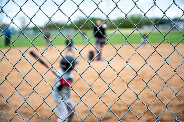 Selective focus on chain link fence with a youth baseball game defocused and blurred in the background. High quality photo