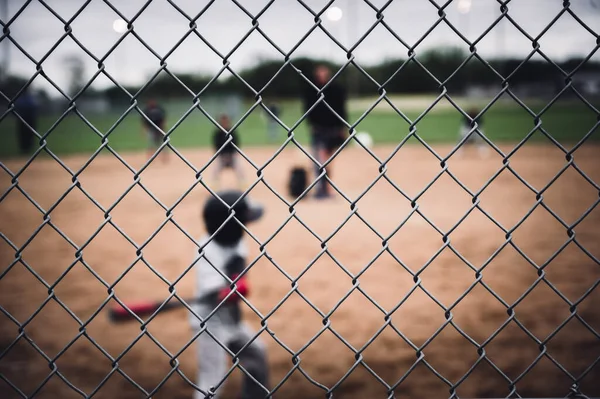 Selective focus on chain link fence with a youth baseball game defocused and blurred in the background. High quality photo