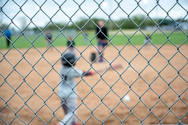 Selective focus on chain link fence with a youth baseball game defocused and blurred in the background. High quality photo