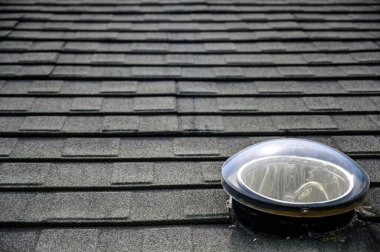 Dome shaped solar tube skylight on asphalt shingle roof . High quality photo