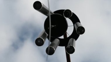 Looking up to the sky underneath a spinning wind chime as the bars are struck. 