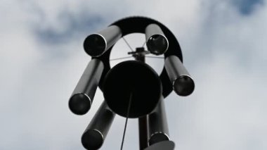 Looking up to the sky underneath a spinning wind chime as the bars are struck. 