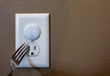 Concept of risk and hazards associated with uncovered electrical outlets with a sharp metal object that could be inserted and cause a shock. clipart