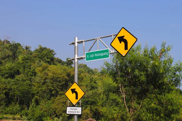 インドネシア西ジャワ州スカブミ2021年6月14日 インドネシアのロジ パランパン スカブミの緑の庭を背景に オレンジの背景と緑の道路標識に警告標識を左折 — ストック写真