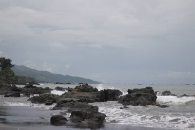 Büyük dalgalar, Citepus plajı Pelabuhan Ratu, Sukabumi, Endonezya 'da dramatik gri bulutlu gökyüzü ile kayalara çarpıyor..