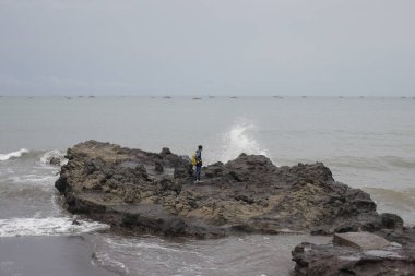 Kayaların üzerinde yürüyen Asyalı bir adam Citepus plajı Pelabuhan Ratu, Sukabumi, Endonezya 'da kayalara çarpıyor..