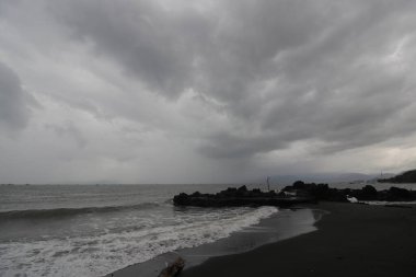 Siyah kumsalda yürüyen ve dalgalardan kaçan yalnız bir adamın arka görüntüsü. Yalnız ve depresif konsept