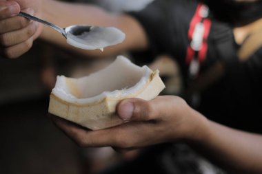 Asyalı bir adam bir kaşık dolusu taze hindistan cevizi yemeye çalışıyor.