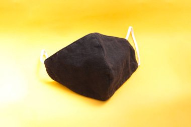 Covid-19 'un turuncu arkaplana yayılmasını önlemek için beyaz kayışlı yeniden kullanılabilir siyah bez maske.