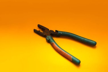 Turuncu arka planda yeşil kabzalı paslı eski pense..