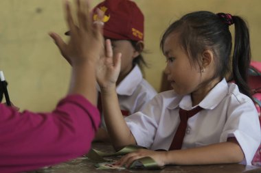 Sumedang, Batı Java, Endonezya - 21 Aralık 2019: Beyaz ve kırmızı üniformalı tatlı bir Endonezyalı ilkokul öğrencisi sınıfta beşlik çakıyor.