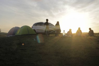 Sukabumi, Batı Java, Endonezya - 14 Mart 2021: Çadırın önünde kahvaltı yapan genç Asyalı gençler ve sabahın sıcacık güneşinde bir çayırda araba