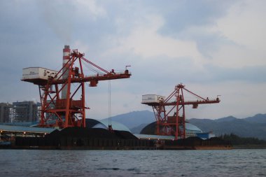 Sukabumi, Batı Java, Endonezya - 23 Ağustos 2021: Kömür ateşiyle çalışan buhar santralinin manzarası kanat vinci ile Pelabuhan Ratu kıyısı yakınlarındaki gemi kargosundan kömür stoklarını kaldırıyor..