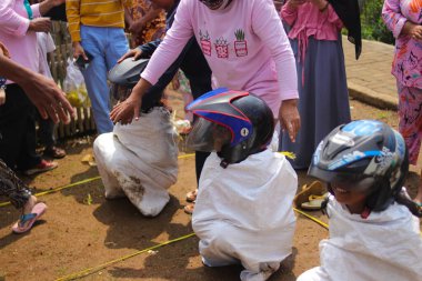 Sukabumi, Batı Java, Endonezya - 19 Ağustos 2021: Endonezyalı miğferli bir grup çocuk Endonezya 'nın Bağımsızlık Günü' nde Balap Karung veya Sack Race adlı geleneksel oyunlarıyla mücadele ediyor