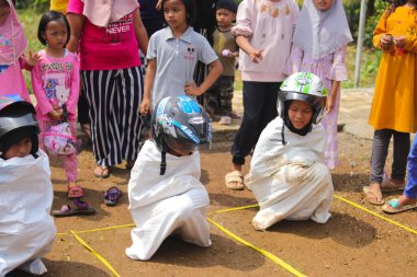 Sukabumi, Batı Java, Endonezya - 19 Ağustos 2021: Endonezyalı miğferli bir grup çocuk Endonezya 'nın Bağımsızlık Günü' nde Balap Karung veya Sack Race adlı geleneksel oyunlarıyla mücadele ediyor