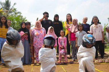 Sukabumi, Batı Java, Endonezya - 19 Ağustos 2021: Endonezyalı miğferli bir grup çocuk Endonezya 'nın Bağımsızlık Günü' nde Balap Karung veya Sack Race adlı geleneksel oyunlarıyla mücadele ediyor