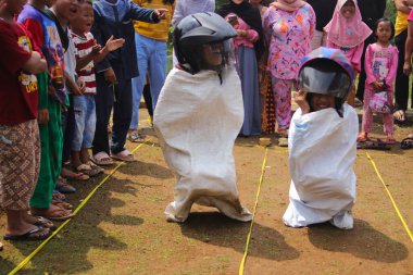 Sukabumi, Batı Java, Endonezya - 19 Ağustos 2021: Endonezyalı miğferli bir grup çocuk Endonezya 'nın Bağımsızlık Günü' nde Balap Karung veya Sack Race adlı geleneksel oyunlarıyla mücadele ediyor
