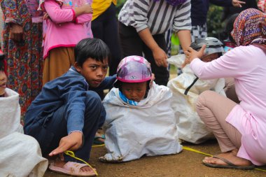 Sukabumi, Batı Java, Endonezya - 19 Ağustos 2021: Endonezyalı miğferli bir grup çocuk Endonezya 'nın Bağımsızlık Günü' nde Balap Karung veya Sack Race adlı geleneksel oyunlarıyla mücadele ediyor