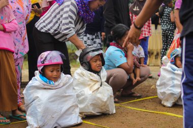 Sukabumi, Batı Java, Endonezya - 19 Ağustos 2021: Endonezyalı miğferli bir grup çocuk Endonezya 'nın Bağımsızlık Günü' nde Balap Karung veya Sack Race adlı geleneksel oyunlarıyla mücadele ediyor