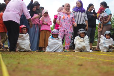 Sukabumi, Batı Java, Endonezya - 19 Ağustos 2021: Endonezyalı miğferli bir grup çocuk Endonezya 'nın Bağımsızlık Günü' nde Balap Karung veya Sack Race adlı geleneksel oyunlarıyla mücadele ediyor