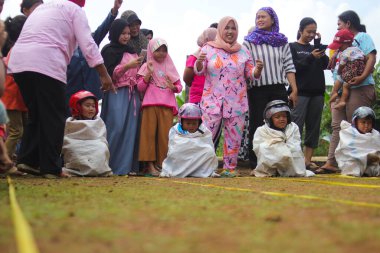 Sukabumi, Batı Java, Endonezya - 19 Ağustos 2021: Endonezyalı miğferli bir grup çocuk Endonezya 'nın Bağımsızlık Günü' nde Balap Karung veya Sack Race adlı geleneksel oyunlarıyla mücadele ediyor