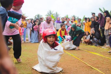 Sukabumi, Batı Java, Endonezya - 19 Ağustos 2021: Endonezyalı miğferli bir grup çocuk Endonezya 'nın Bağımsızlık Günü' nde Balap Karung veya Sack Race adlı geleneksel oyunlarıyla mücadele ediyor