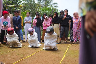 Sukabumi, Batı Java, Endonezya - 19 Ağustos 2021: Endonezyalı miğferli bir grup çocuk Endonezya 'nın Bağımsızlık Günü' nde Balap Karung veya Sack Race adlı geleneksel oyunlarıyla mücadele ediyor