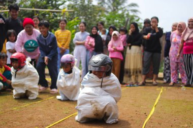Sukabumi, Batı Java, Endonezya - 19 Ağustos 2021: Endonezyalı miğferli bir grup çocuk Endonezya 'nın Bağımsızlık Günü' nde Balap Karung veya Sack Race adlı geleneksel oyunlarıyla mücadele ediyor