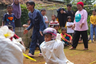 Sukabumi, Batı Java, Endonezya - 19 Ağustos 2021: Endonezyalı miğferli bir grup çocuk Endonezya 'nın Bağımsızlık Günü' nde Balap Karung veya Sack Race adlı geleneksel oyunlarıyla mücadele ediyor