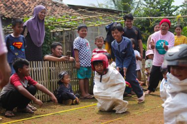 Sukabumi, Batı Java, Endonezya - 19 Ağustos 2021: Endonezyalı miğferli bir grup çocuk Endonezya 'nın Bağımsızlık Günü' nde Balap Karung veya Sack Race adlı geleneksel oyunlarıyla mücadele ediyor