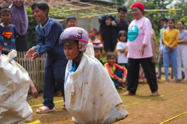Sukabumi, Batı Java, Endonezya - 19 Ağustos 2021: Endonezyalı miğferli bir grup çocuk Endonezya 'nın Bağımsızlık Günü' nde Balap Karung veya Sack Race adlı geleneksel oyunlarıyla mücadele ediyor