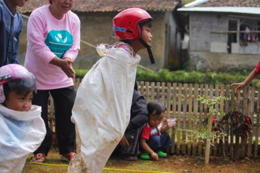 Sukabumi, Batı Java, Endonezya - 19 Ağustos 2021: Endonezyalı miğferli bir grup çocuk Endonezya 'nın Bağımsızlık Günü' nde Balap Karung veya Sack Race adlı geleneksel oyunlarıyla mücadele ediyor